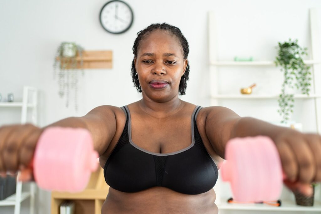 Woman holding pink hand weights while exercising indoors.