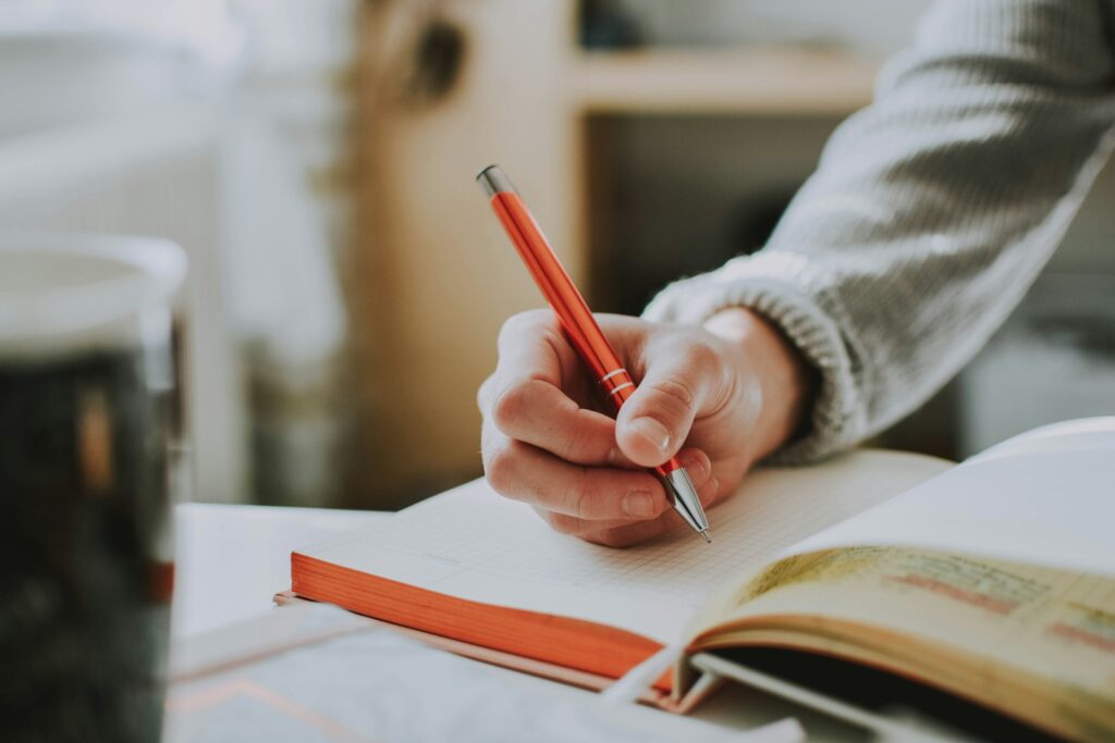 Hand holding a red pen over an open notebook.
