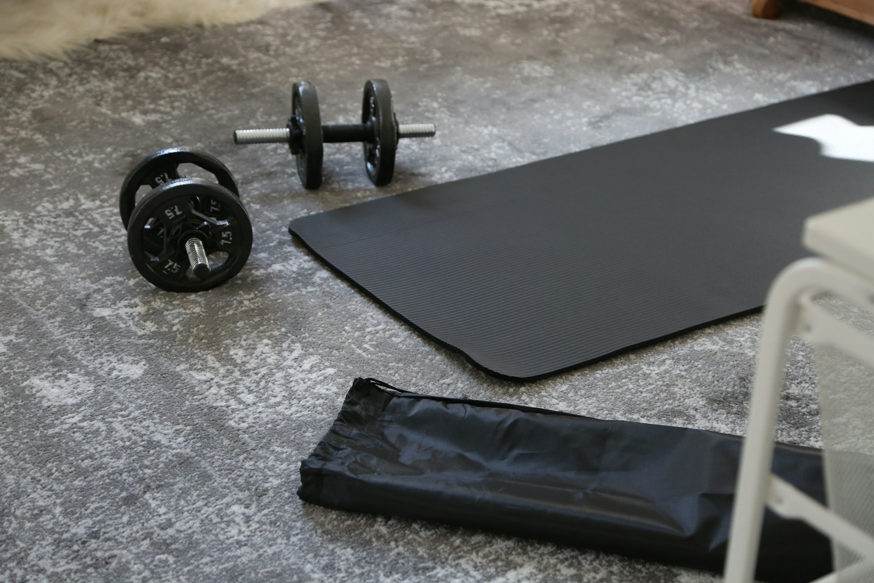 Two dumbbells beside a black exercise mat on a carpeted floor.