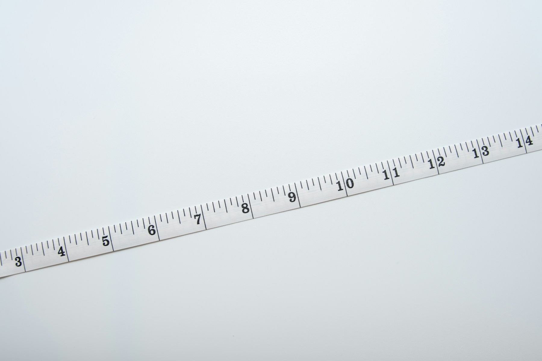 A white centimetre measuring tape lies diagonally across a plain pale surface.
